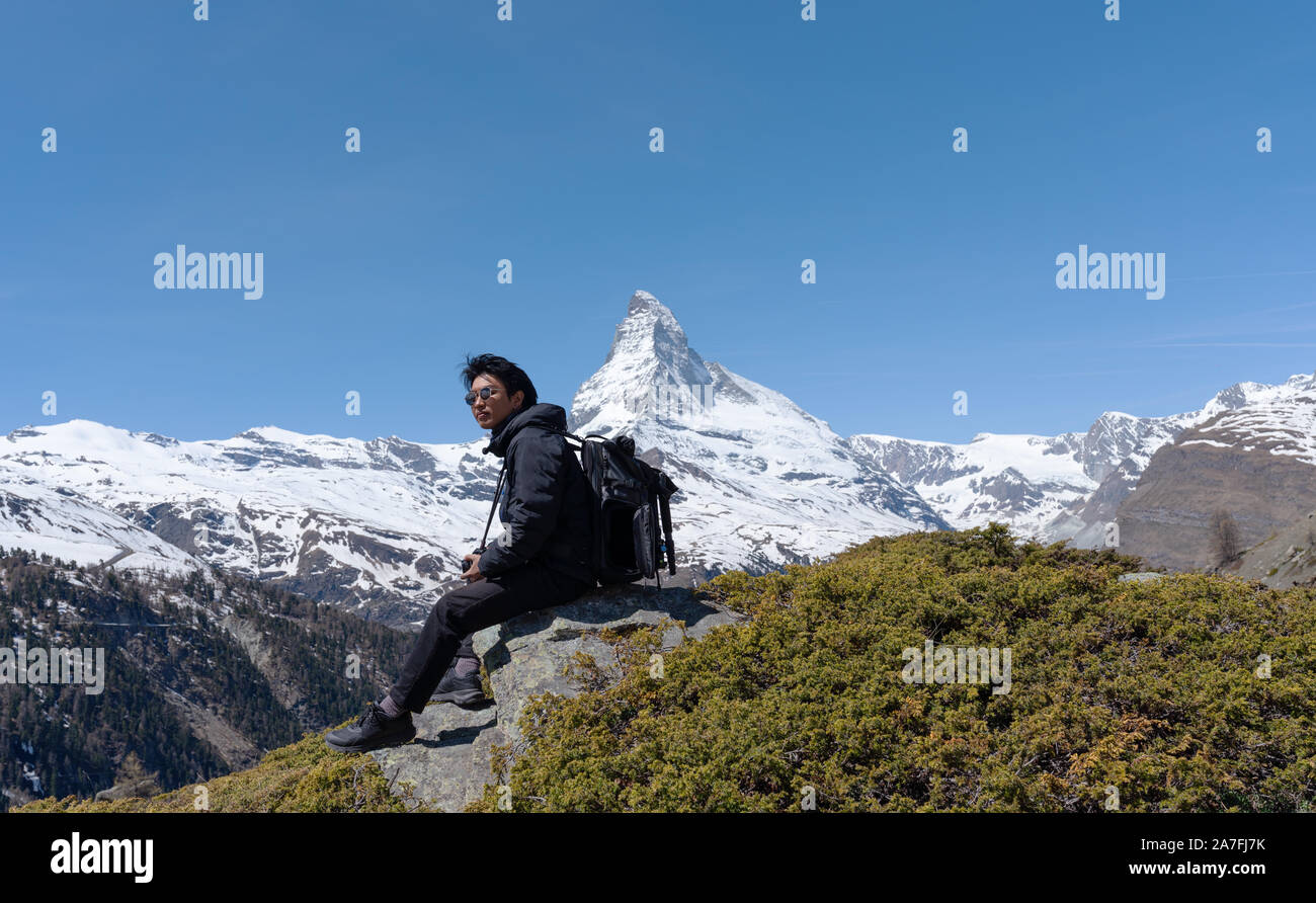 Ein Mann mit Rucksack auf Felsen mit Blick auf das Matterhorn in der Schweiz sitzen Stockfoto
