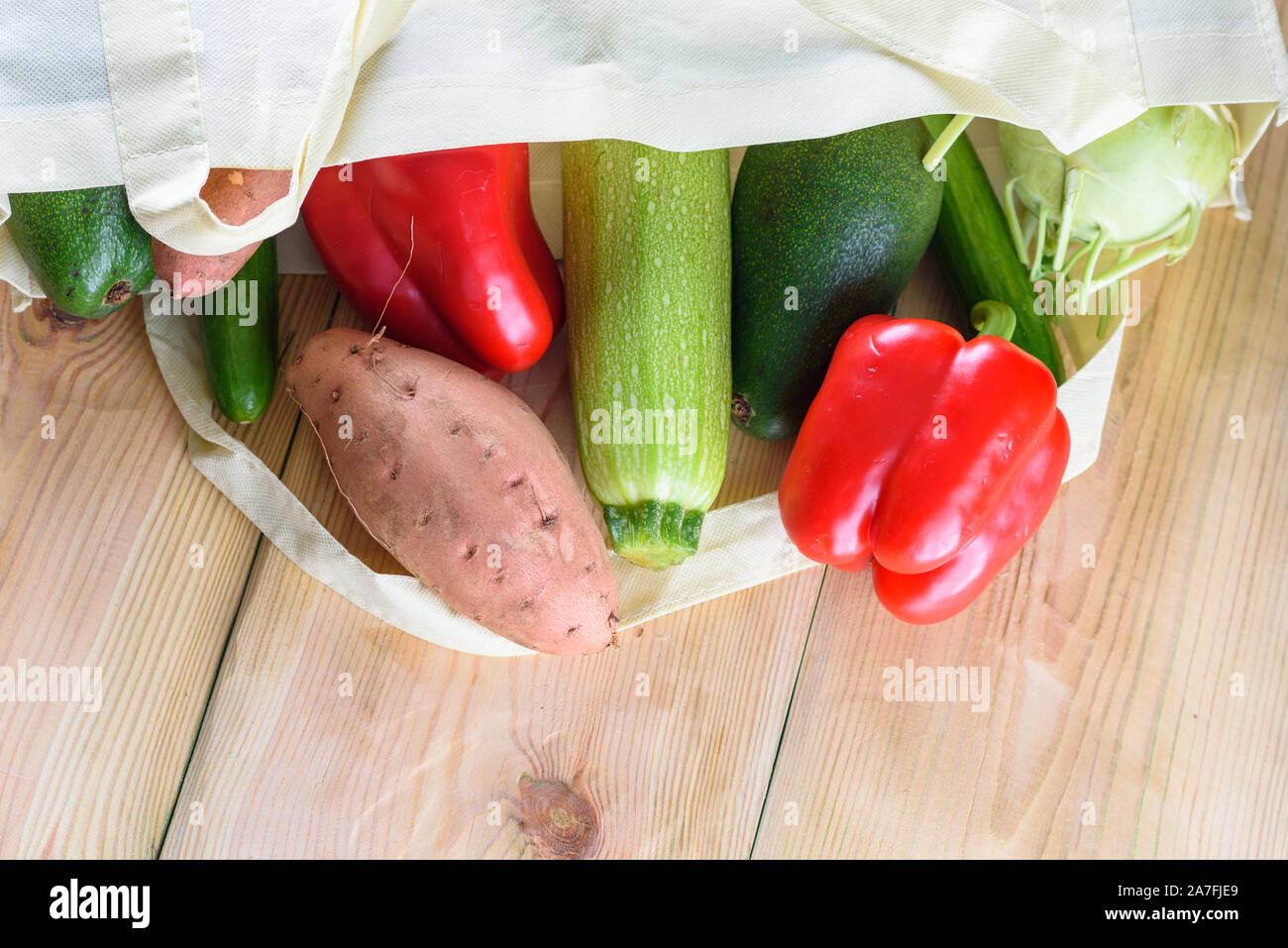 Welt frei von Kunststoff. Wiederverwendbare umweltfreundliche Leinwand einkaufen Tasche mit Gemüse - süsse Kartoffeln, Zucchini, Paprika, Tomaten, Gurke und Avocado auf hölzernen Schreibtisch. Organische Produkte. Weniger Kunststoff. Stockfoto