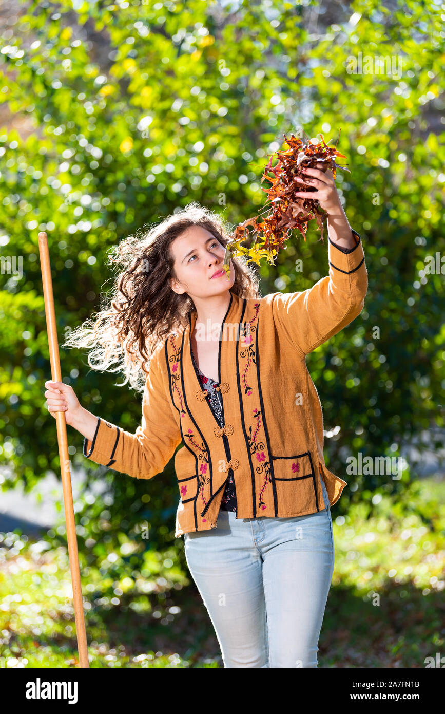 Junge Frau Eigenheimbesitzer im Hof Garten harken Sammeln von trockenen Herbst Laub Eichenlaub ständigen Holding Laub mit Rake im sonnigen Herbst Stockfoto