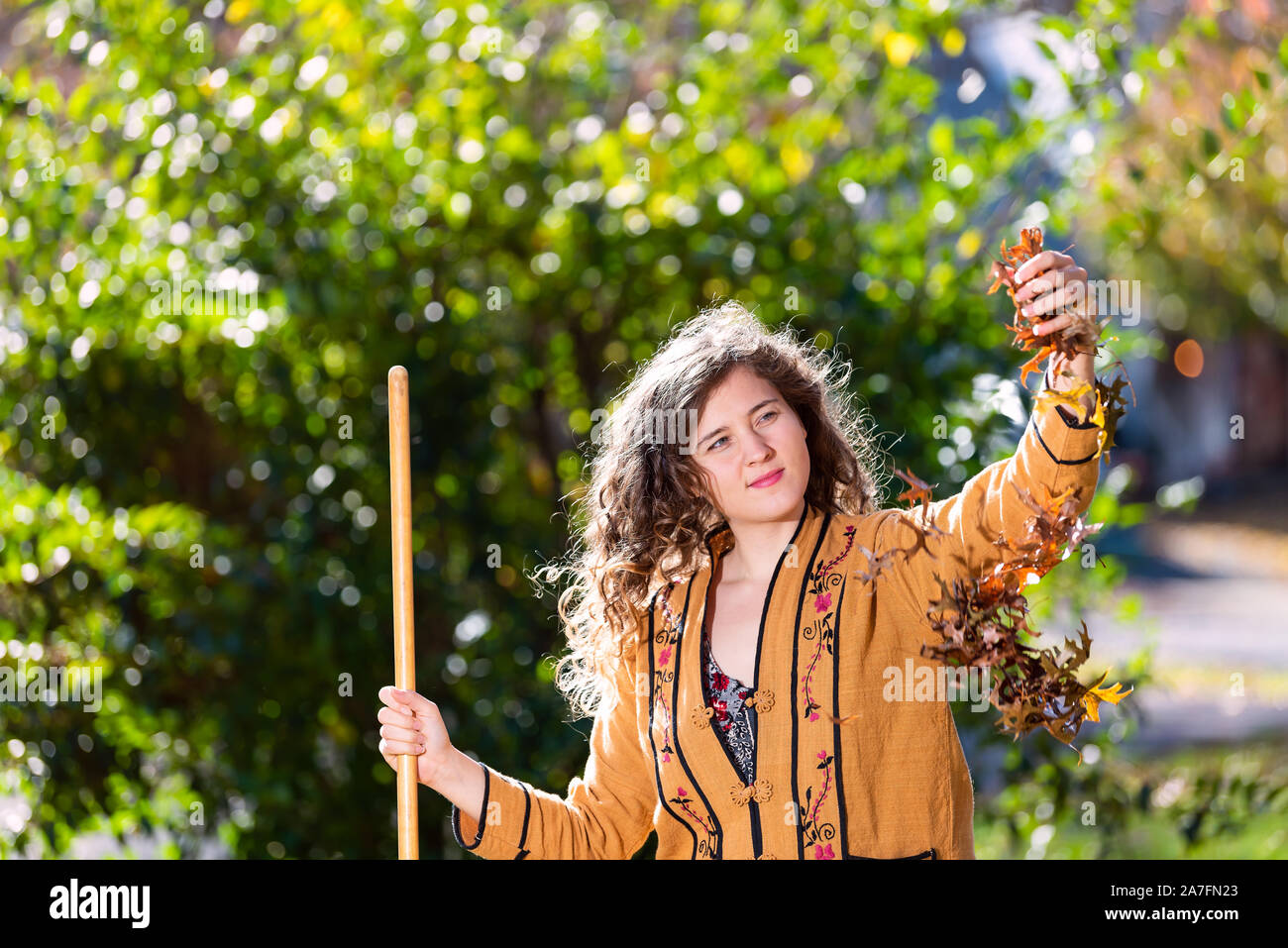 Junge Frau in Yard Hinterhof harken Sammeln von trockenen Herbst Laub Eichenlaub ständigen Holding Laub fällt mit Rechen im sonnigen Herbst Stockfoto