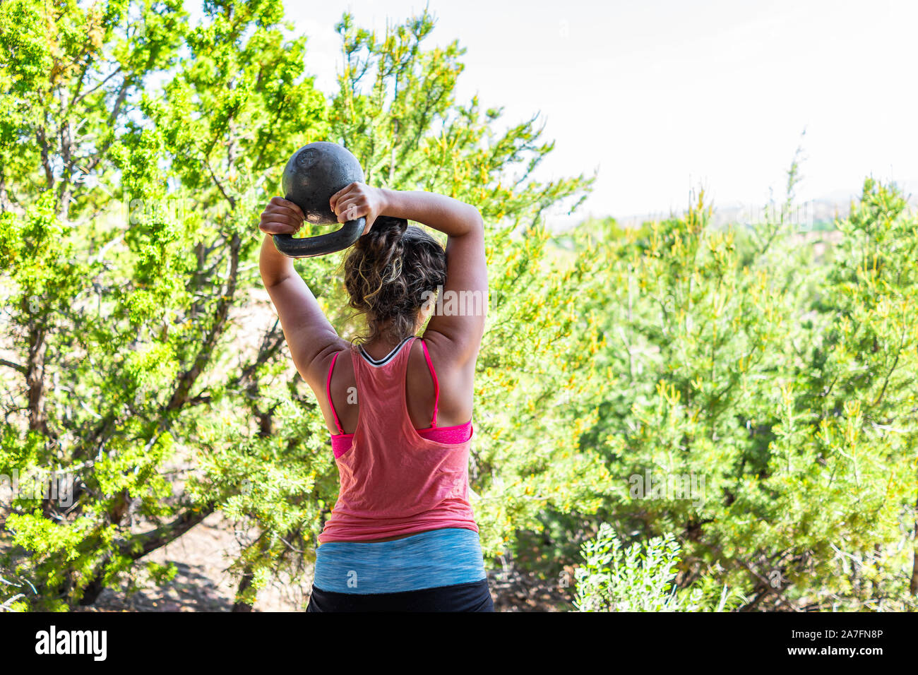 Zurück junger passende Frau mit schweren kettlebell tun Trizeps übung und Muskeln im Freien außerhalb Park holding Gewichtheben Stockfoto