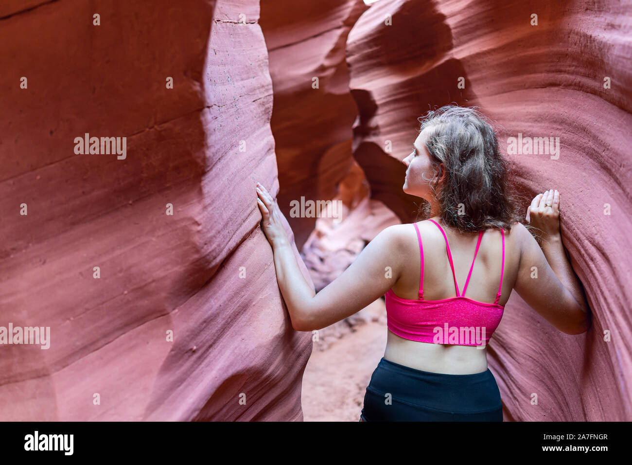 Rückseite der jungen Frau zu Fuß auf Wanderung berühren Formationen Wellenformen auf engen Antelope Slot Canyon in Arizona im Sommer mit Sport-BH Stockfoto