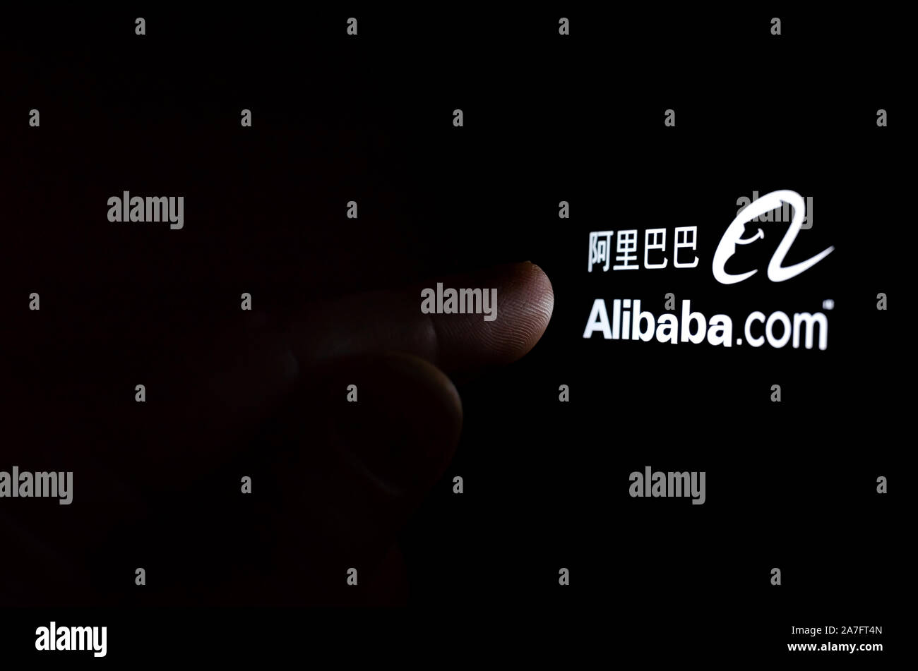 Alibaba Firmenlogo auf einem Bildschirm des Smartphones in einem dunklen Raum und einen Finger zu berühren. Stockfoto