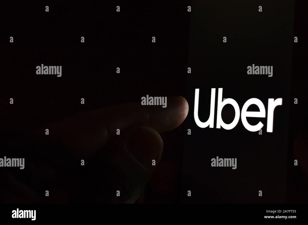 Uber Logo auf einem Bildschirm des Smartphones in einem dunklen Raum und einen Finger zu berühren. Stockfoto