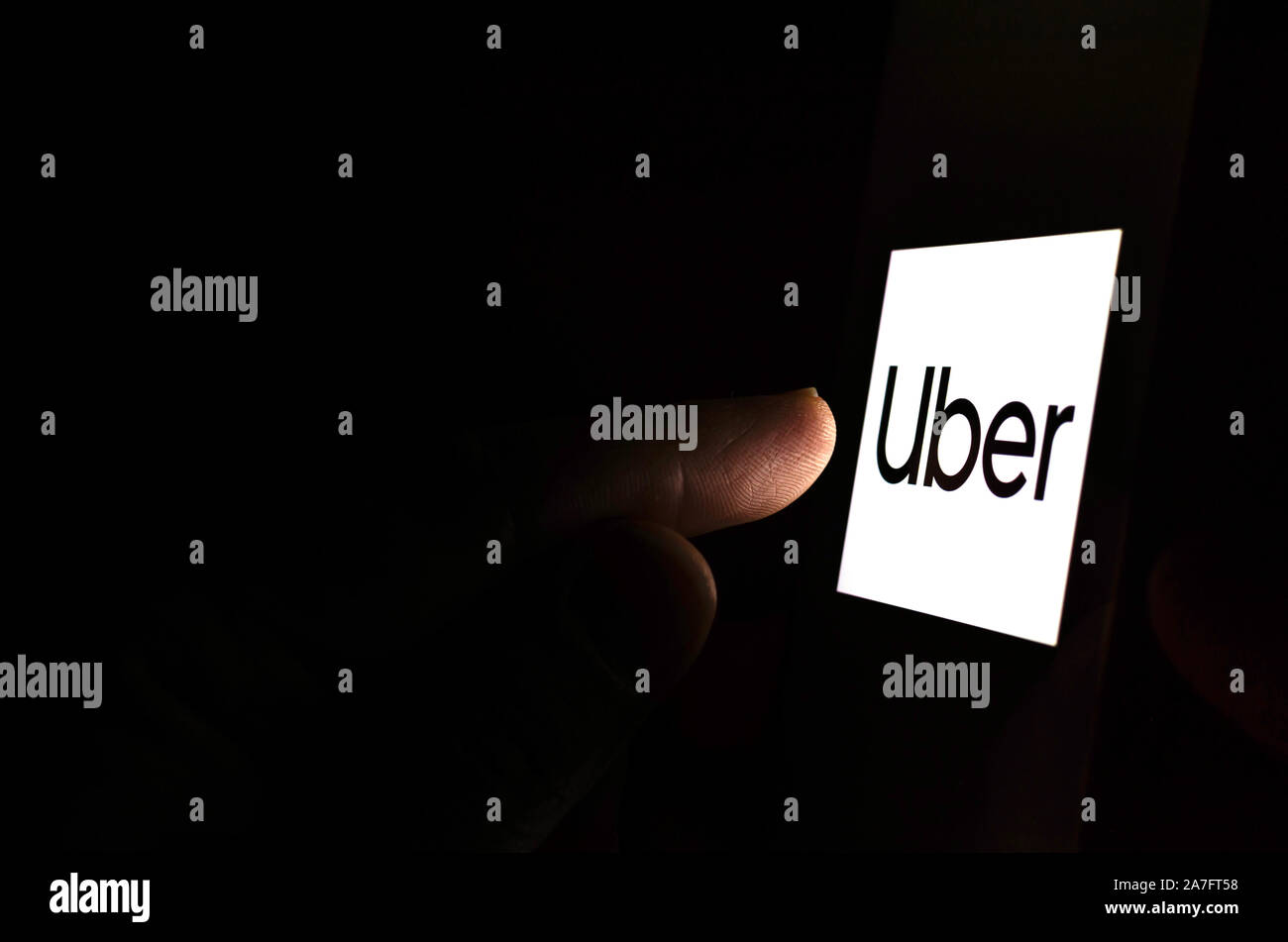 Uber Logo auf einem Bildschirm des Smartphones in einem dunklen Raum und einen Finger zu berühren. Stockfoto