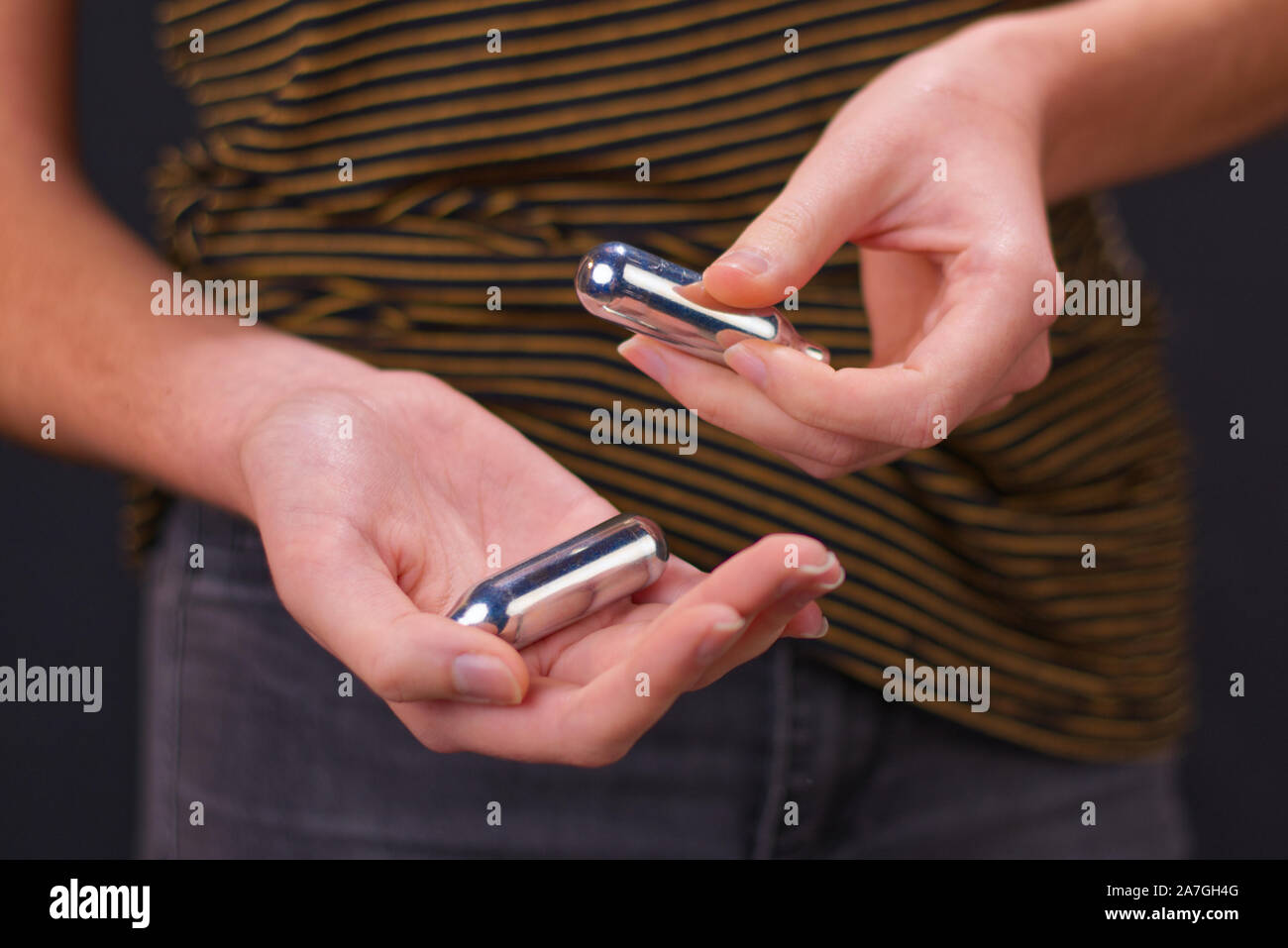 Schönen jungen Mädchen in den engen Jeans, die Lachgas Patronen angezeigt in den Händen. Lachgas ist gefährlicher als Freizeitdroge betrachtet. Stockfoto