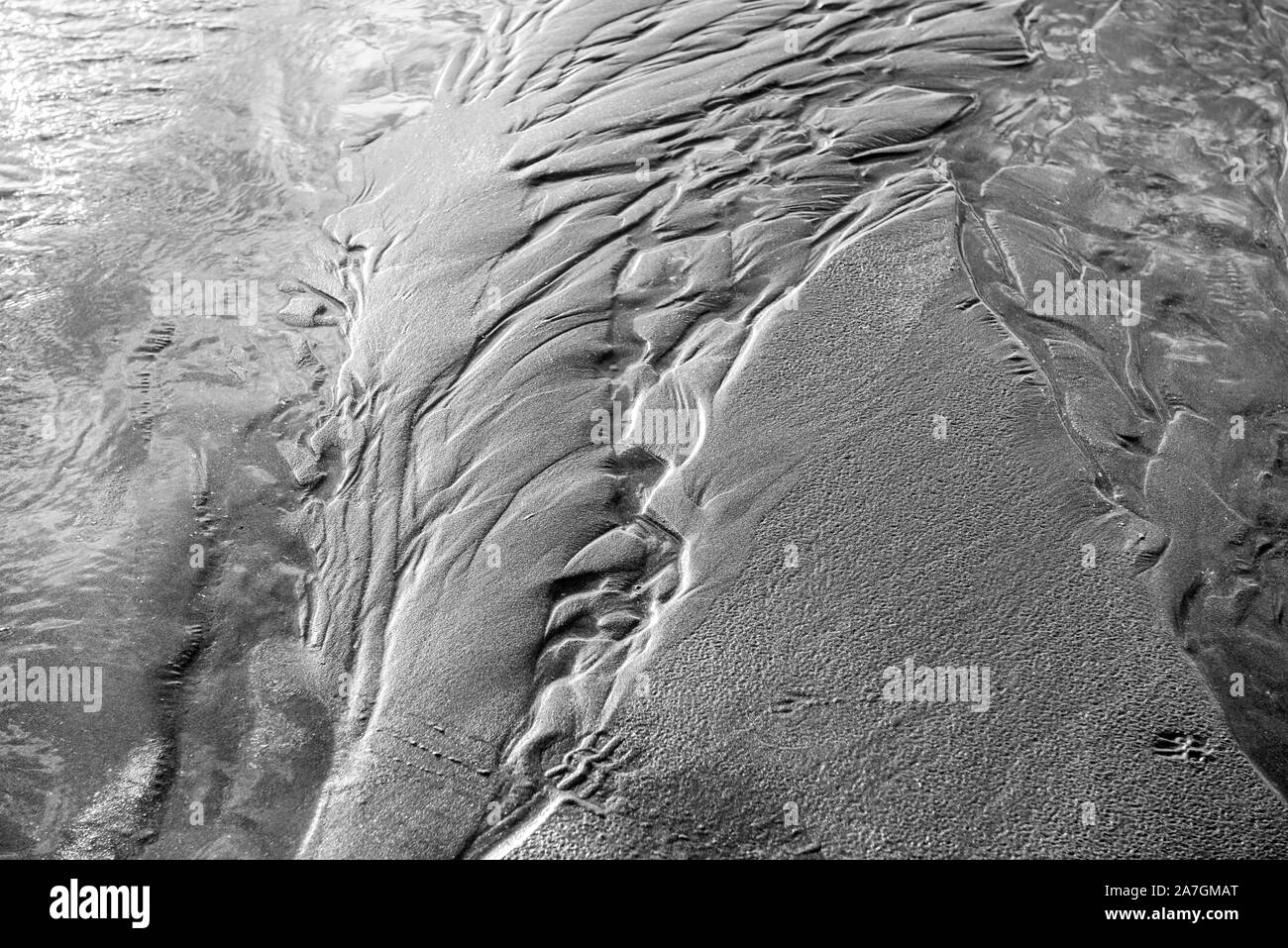 Bewegtes Wasser über Sand in Schwarzweiß mit leichten Wellen und ein wenig Bewegung Bewegungsunschärfe Bewegung zu zeigen. Schöne Textur und Stimmung mit Sand Muster. Stockfoto