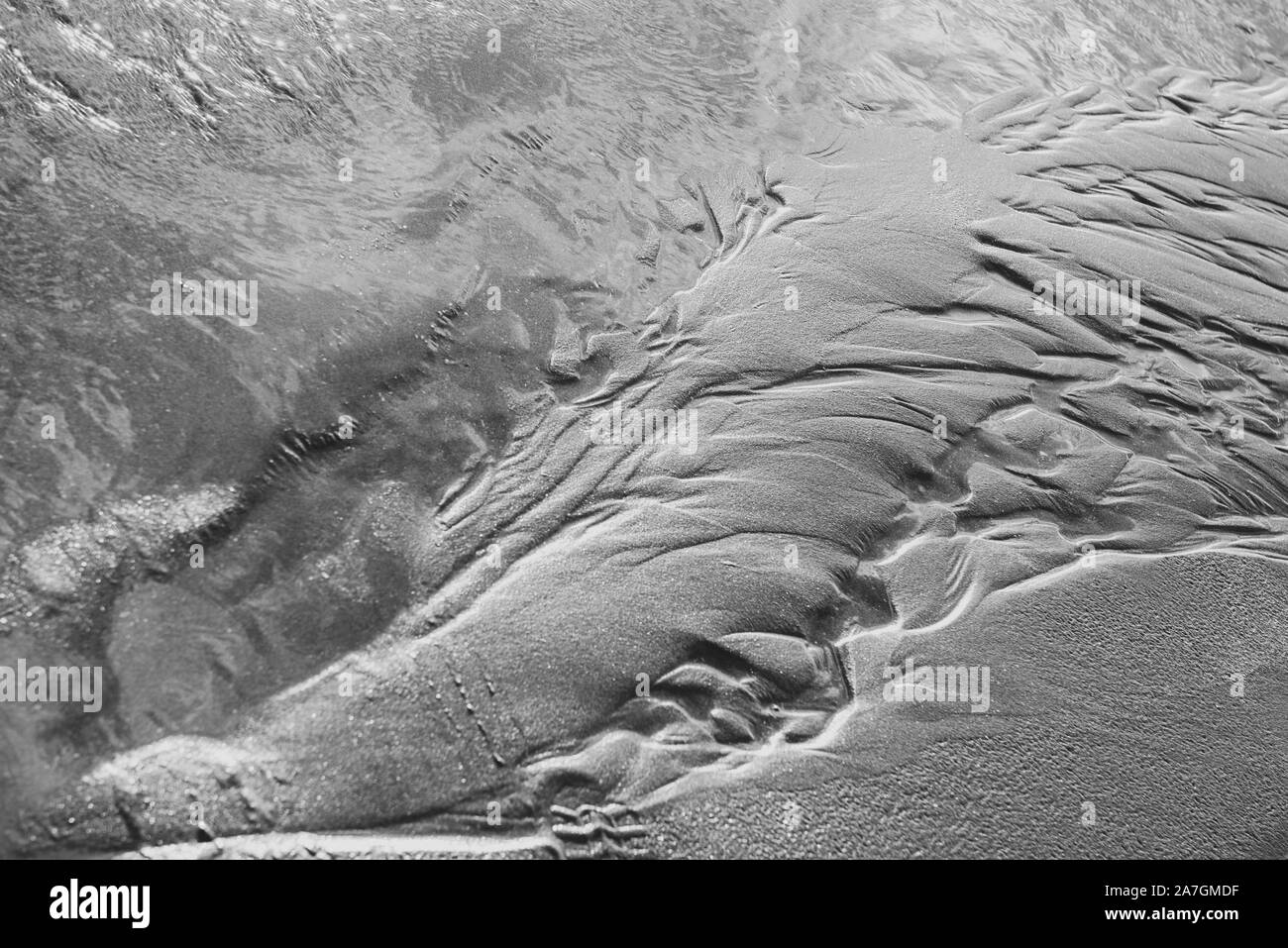 Bewegtes Wasser über Sand in Schwarzweiß mit leichten Wellen und ein wenig Bewegung Bewegungsunschärfe Bewegung zu zeigen. Schöne Textur und Stimmung mit Sand Muster. Stockfoto