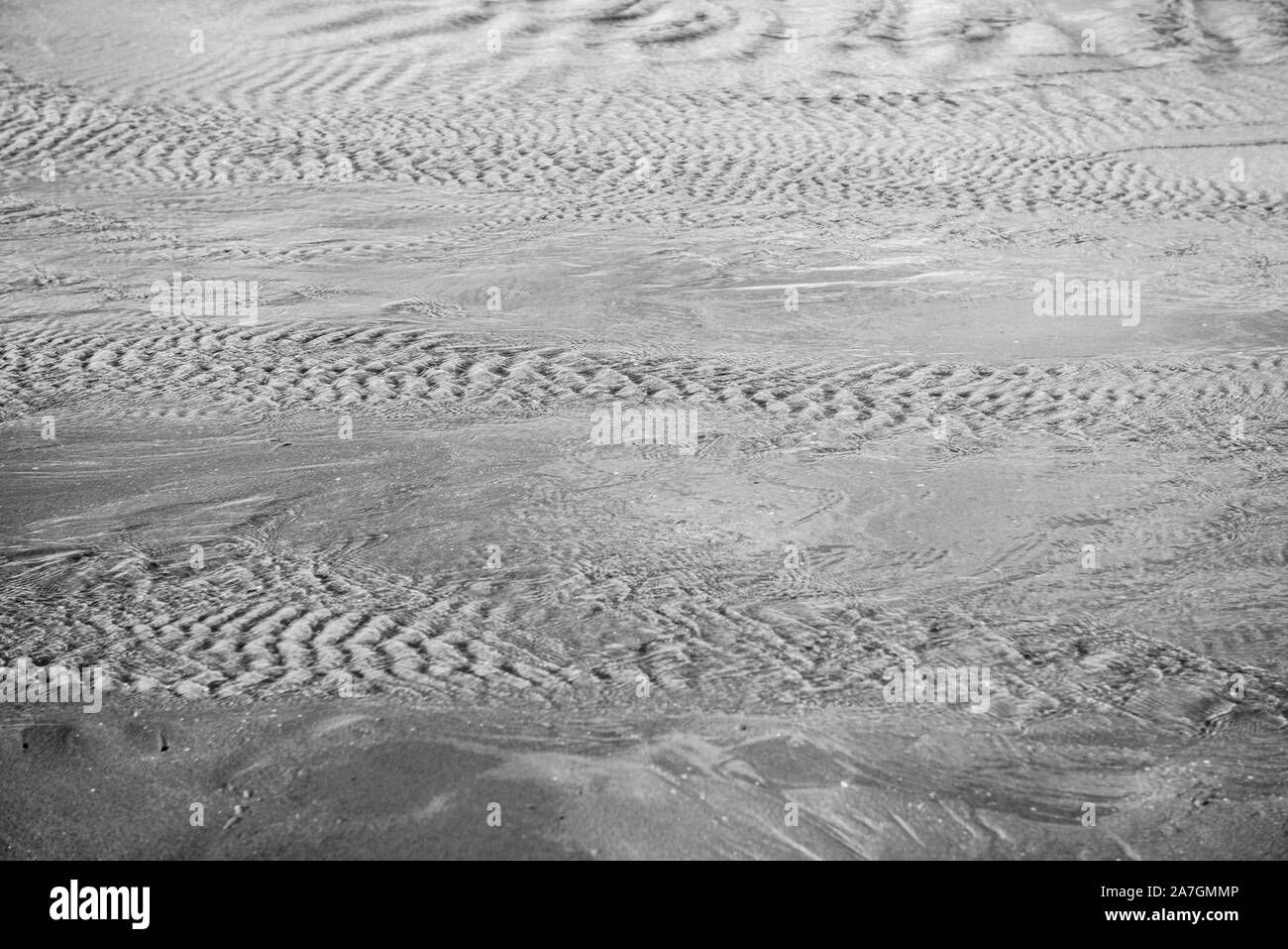 Bewegtes Wasser über Sand in Schwarzweiß mit leichten Wellen und ein wenig Bewegung Bewegungsunschärfe Bewegung zu zeigen. Schöne Textur und Stimmung mit Sand Muster. Stockfoto