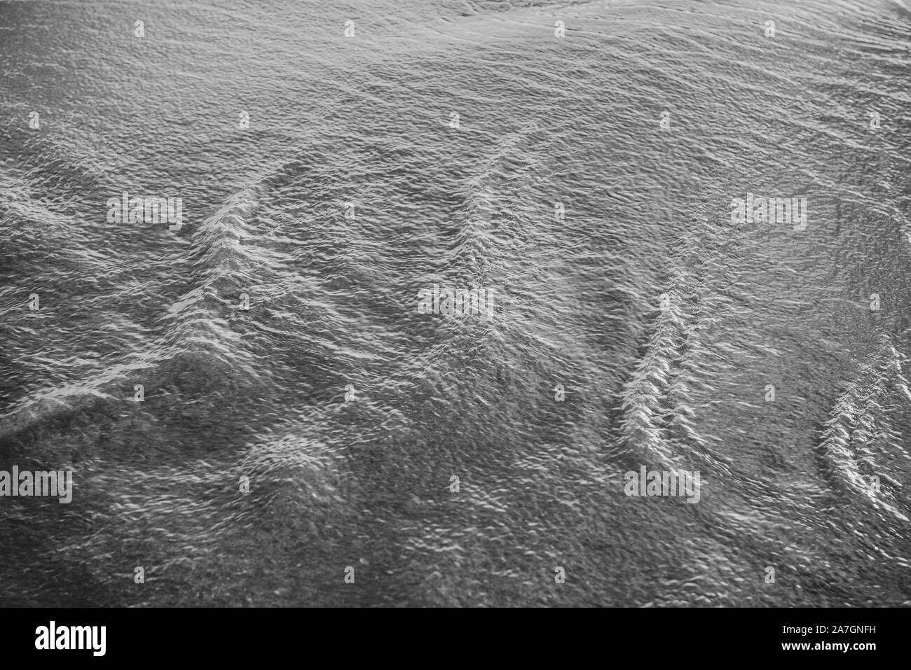 Bewegtes Wasser über Sand bei kontrastreichen Schwarzweiß-Bild mit leichten Wellen und ein wenig Bewegung Bewegungsunschärfe Bewegung zu zeigen. Schöne Textur und Stimmung. Stockfoto