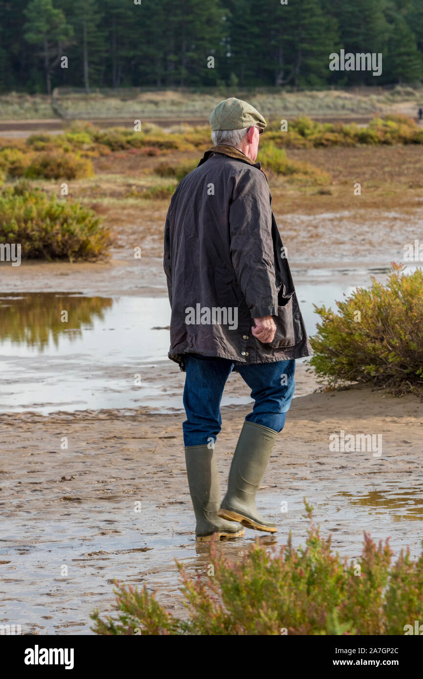 Land gentleman Landwirt tragen gewachsten Jacke und grüne Gummistiefel oder  wellies und flache Tweed Cap Wandern auf nassen Sumpfgebiet Stockfotografie  - Alamy