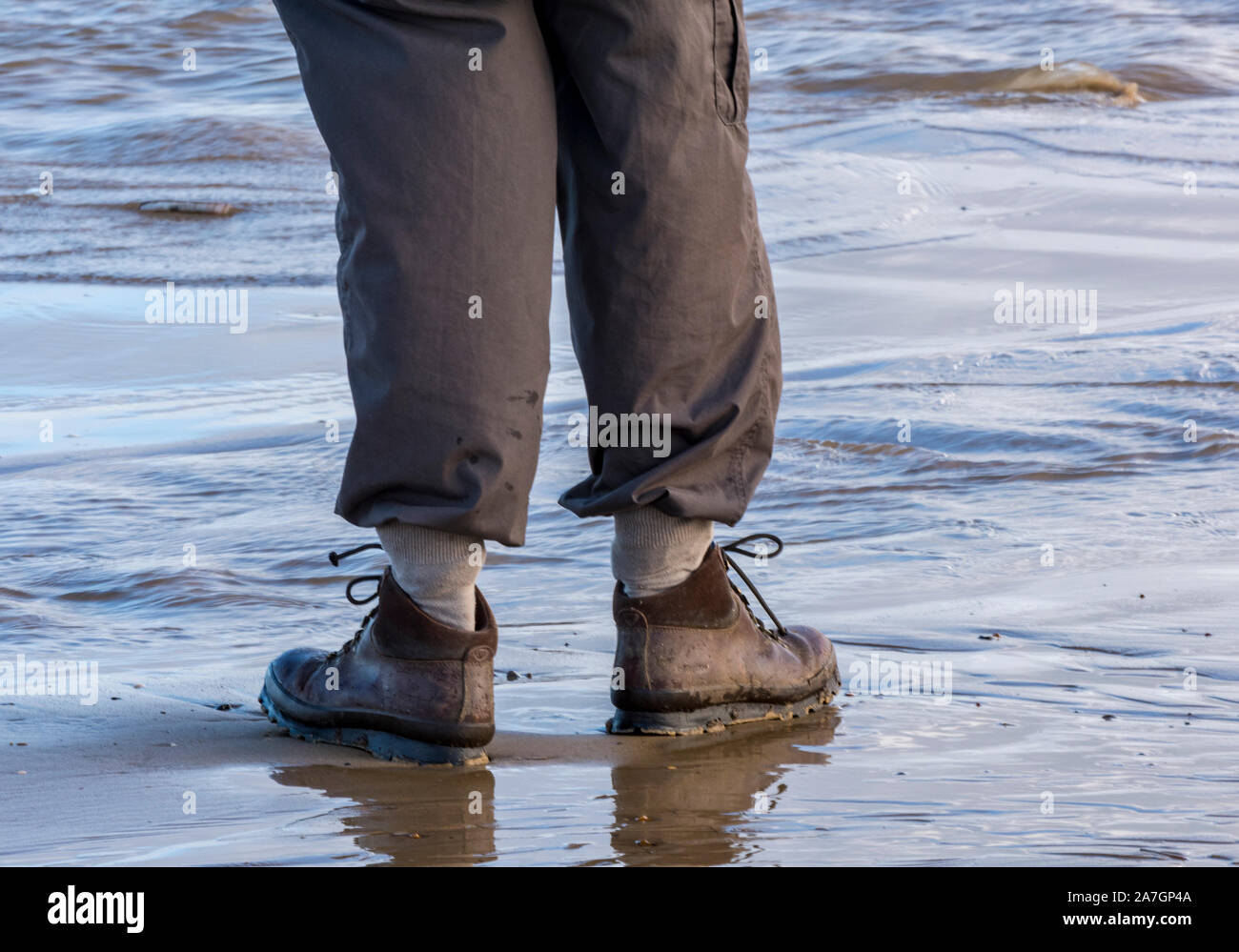 Mann, der ein Paar Stiefel zum laufen trägt. Feuchter Strand mit Hose, die in Socken auf nassem Sand am heiligen Schinken, norfolk, Deutschland, versteckt ist Stockfoto