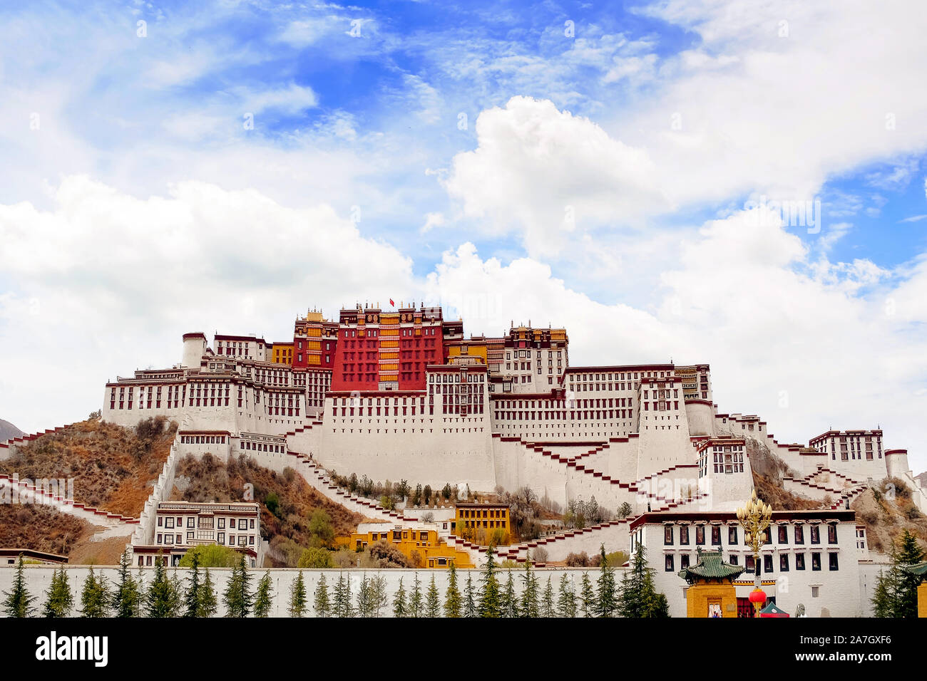 Vorderansicht des Potala Palast in Lhasa, Tibet, von grüner Vegetation, gegen einen blauem Himmel mit weißen Wolken bedeckt. Stockfoto