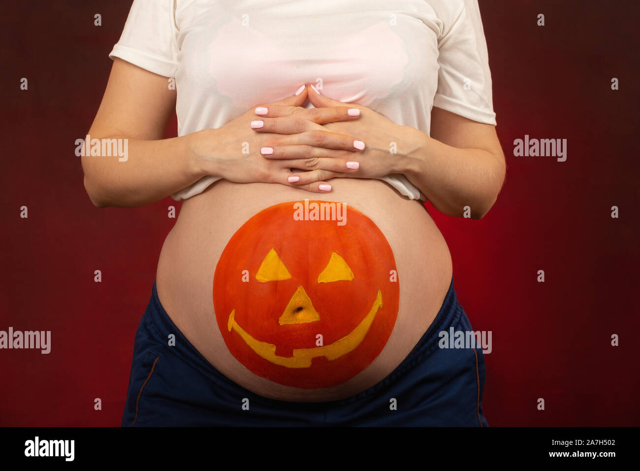 Junge schwangere Frau mit Kürbis Halloween auf dem Bauch Closeup Portrait gemalt Stockfoto