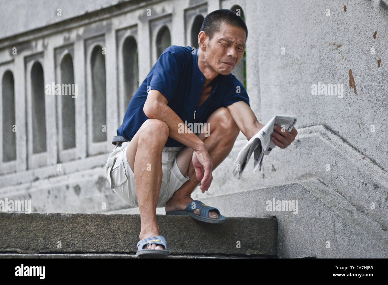 Chinesischer Mann hocken und die Zeitung lesen. Changjiang Brücke, Wuhan, China Stockfoto