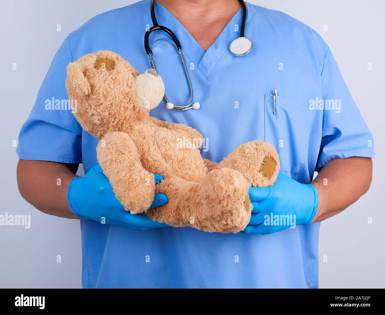 Arzt in der blauen Uniform und dem weißen Latex Handschuhe mit einem braunen Teddybär, Kinderheilkunde Konzept Stockfoto