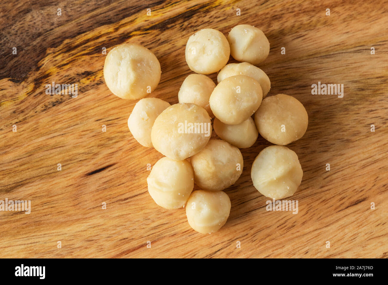 Eine Handvoll Macadamia Nüsse ohne Schale, leicht geröstet und mit ein wenig Salz, von oben fotografiert, auf einer Mango Holz. Stockfoto