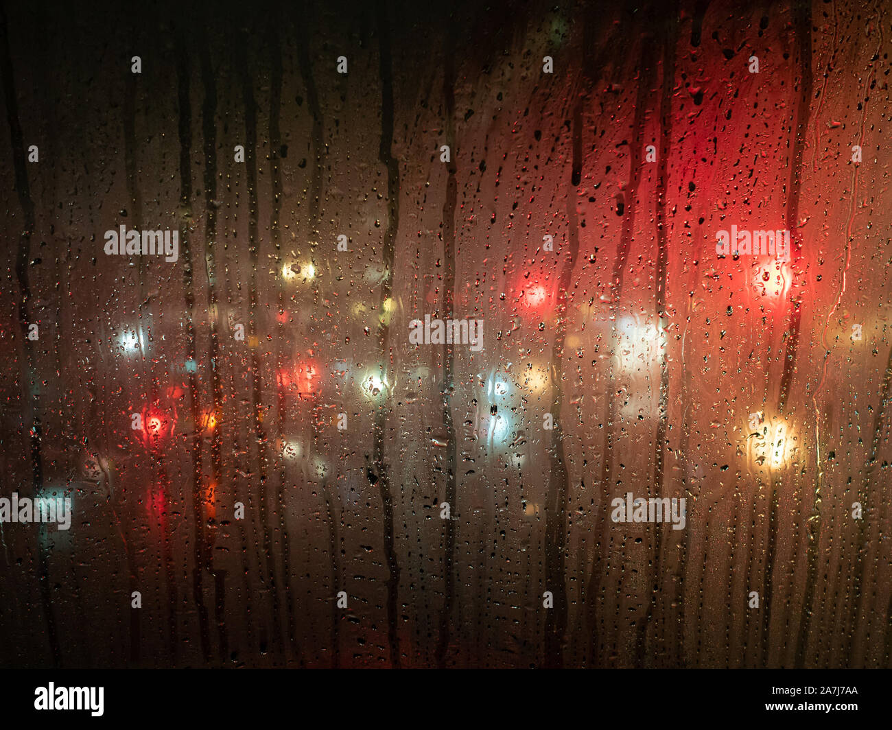 Regentropfen auf einem Bus-Fenster mit unscharfen Scheinwerfer hinter Stockfoto