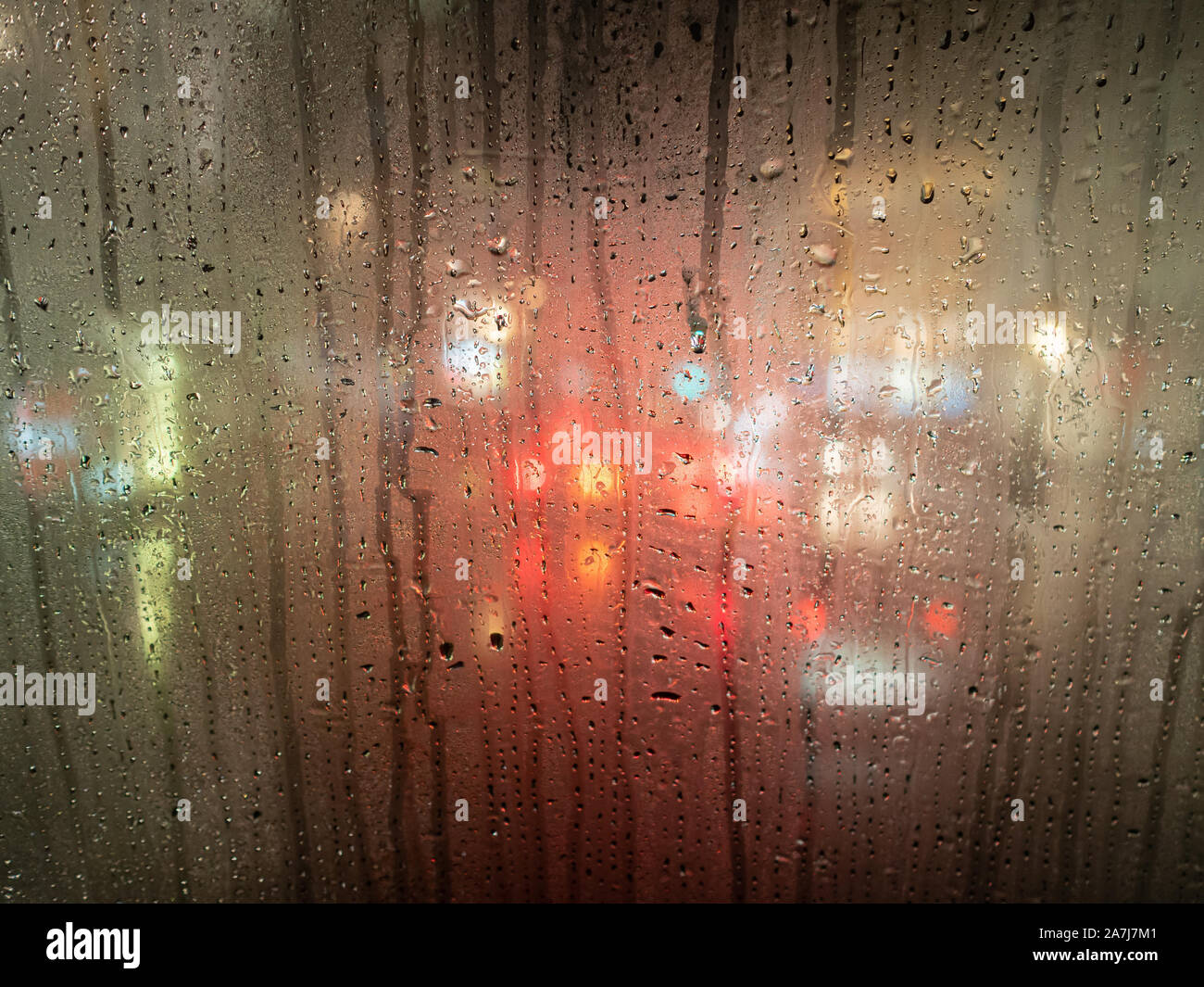 Regentropfen auf einem Bus-Fenster mit unscharfen Scheinwerfer hinter Stockfoto
