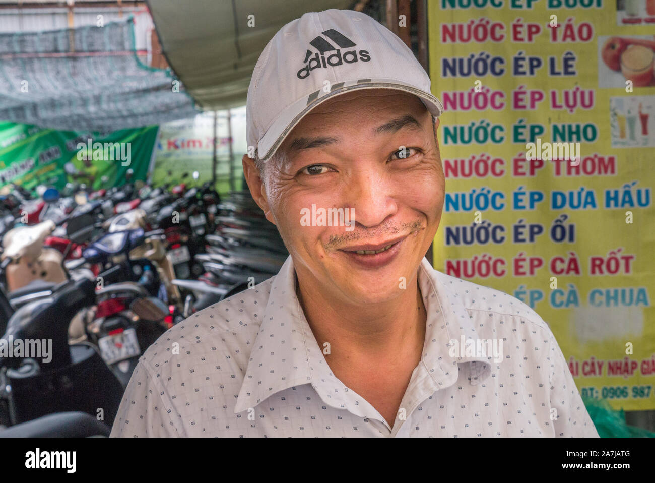 Portrait des grinsenden männlichen vietnamesischen Roller Parkwächters, der vor dem Restaurantfood-Schild mit dicht gepackten Rollern im Hintergrund steht. Stockfoto