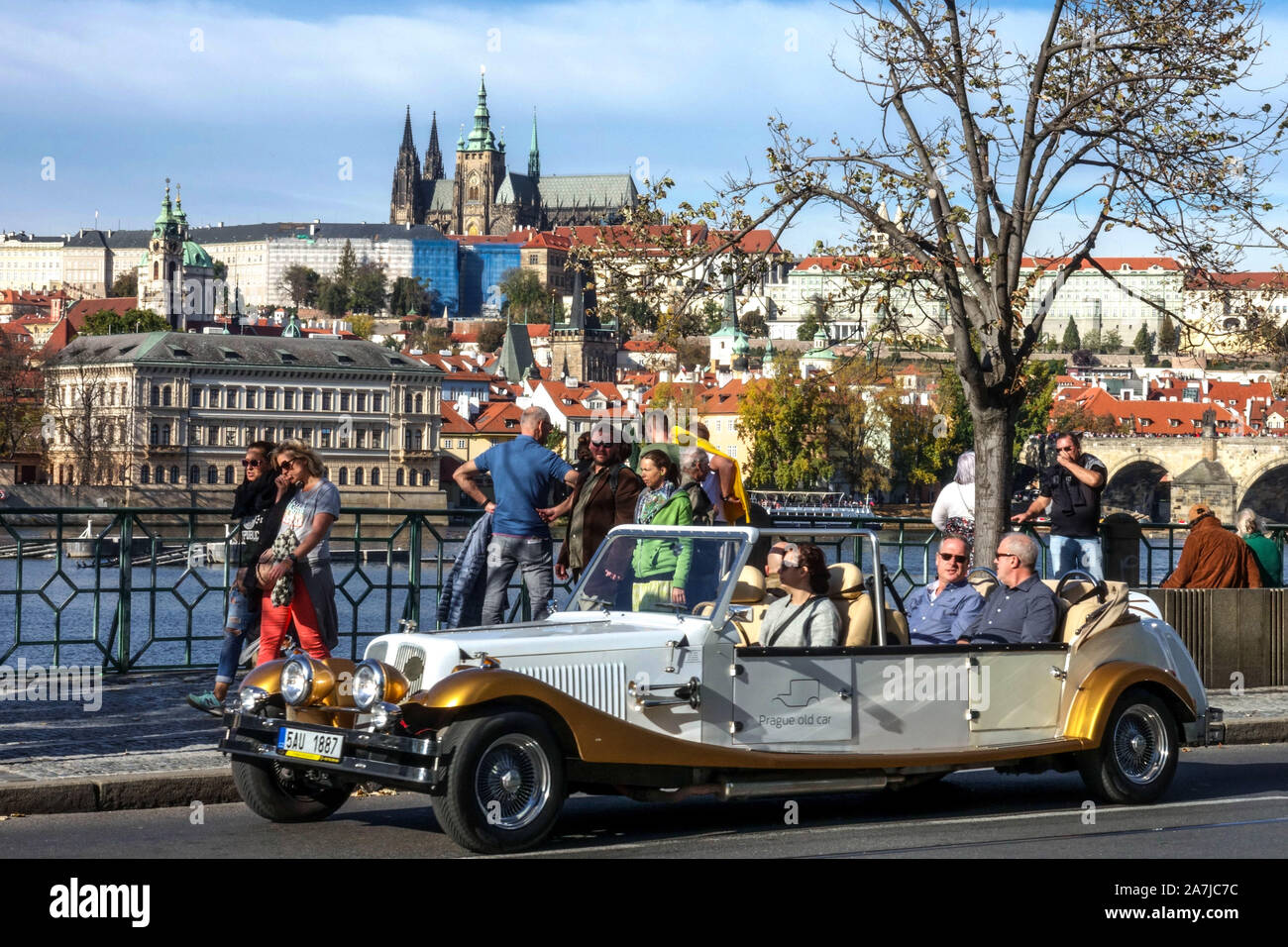 Prager Touristen in Nachahmung Oldtimer Taxi gefälschte Veteranen Auto Leute Smetanovo nabrezi mit Blick auf die Prager Burg Stadt Gebäude über dem Fluss Blick Stockfoto