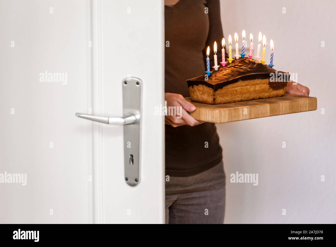 Frau mit Geburtstag Kuchen kommt durch eine weiße Tür Stockfoto