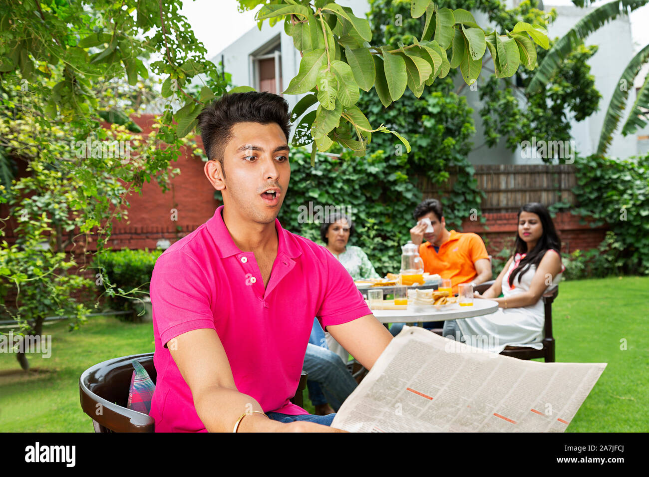 Mann sitzt auf dem Stuhl lesen badnews auf - Zeitung mit der Familie in den Hintergrund im Innenhof ihres Hauses Schockiert Stockfoto