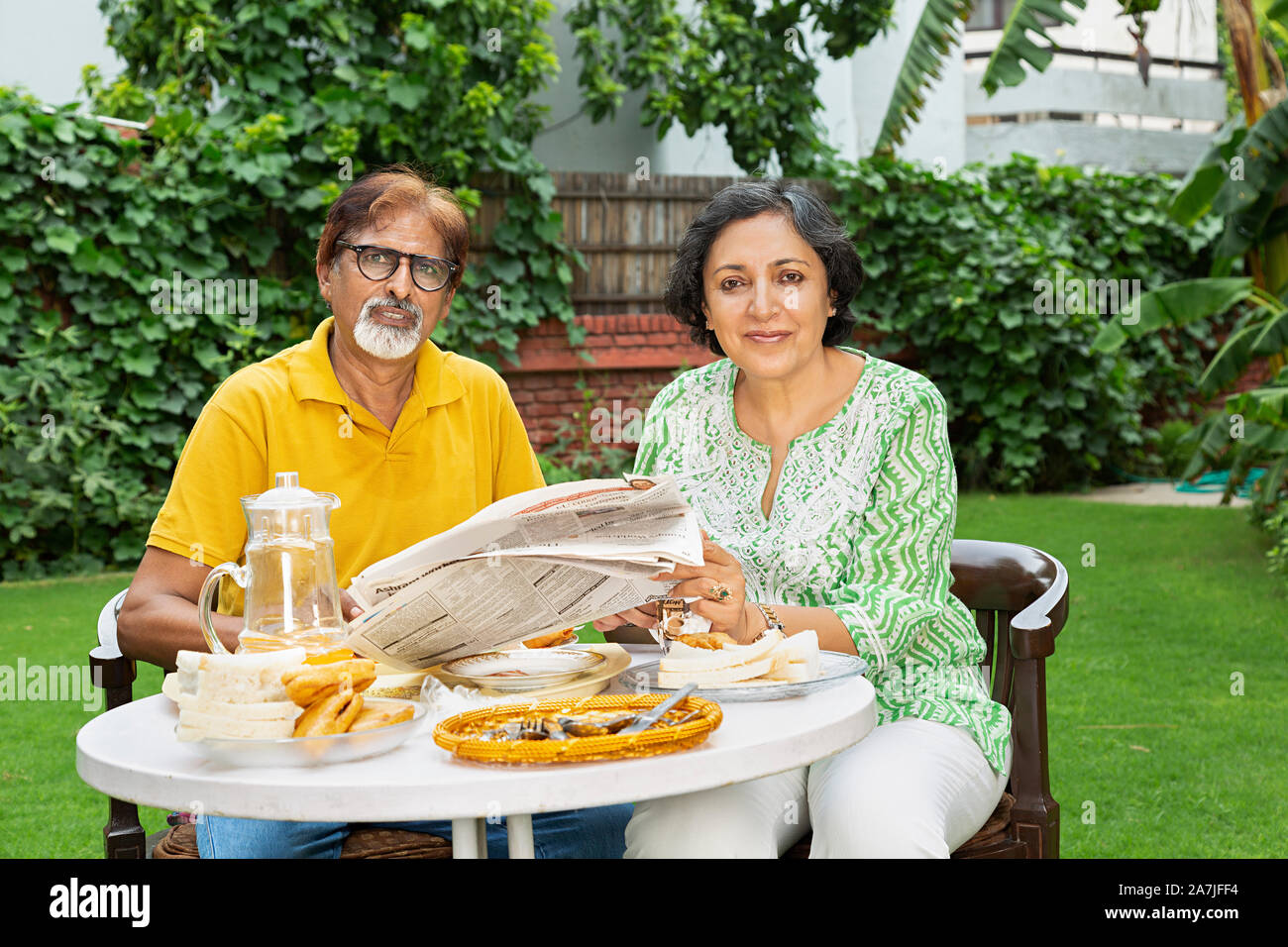 Alte Paar lesen Zeitung zusammen und Frühstücken in Tabelle im Innenhof ihres Hauses Stockfoto