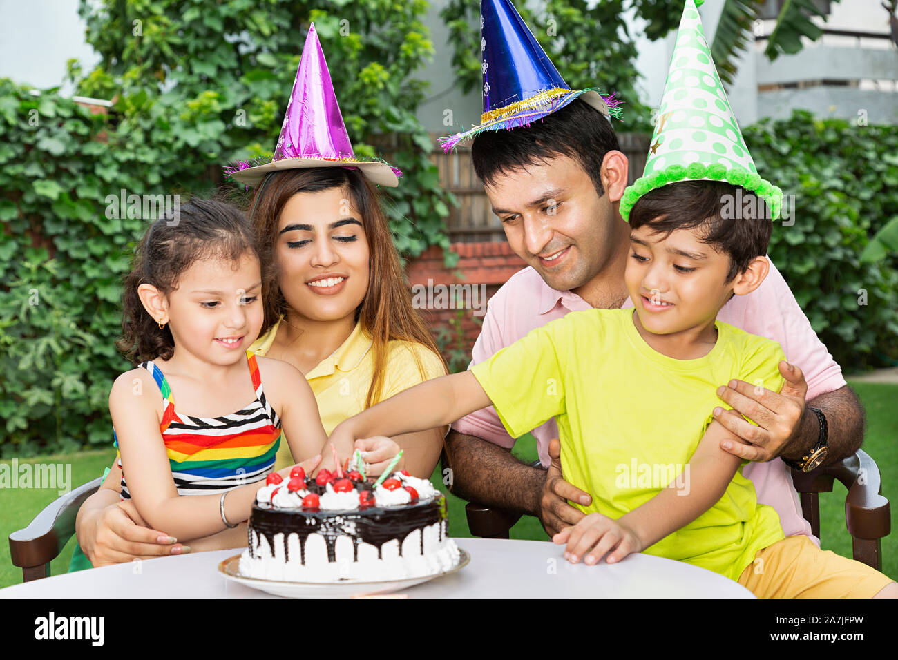 Glückliche junge Familie Kinder Geburtstag feiern Eltern und zwei Kinder gemeinsam feiern im Innenhof in der Nähe Ihres Hauses Stockfoto
