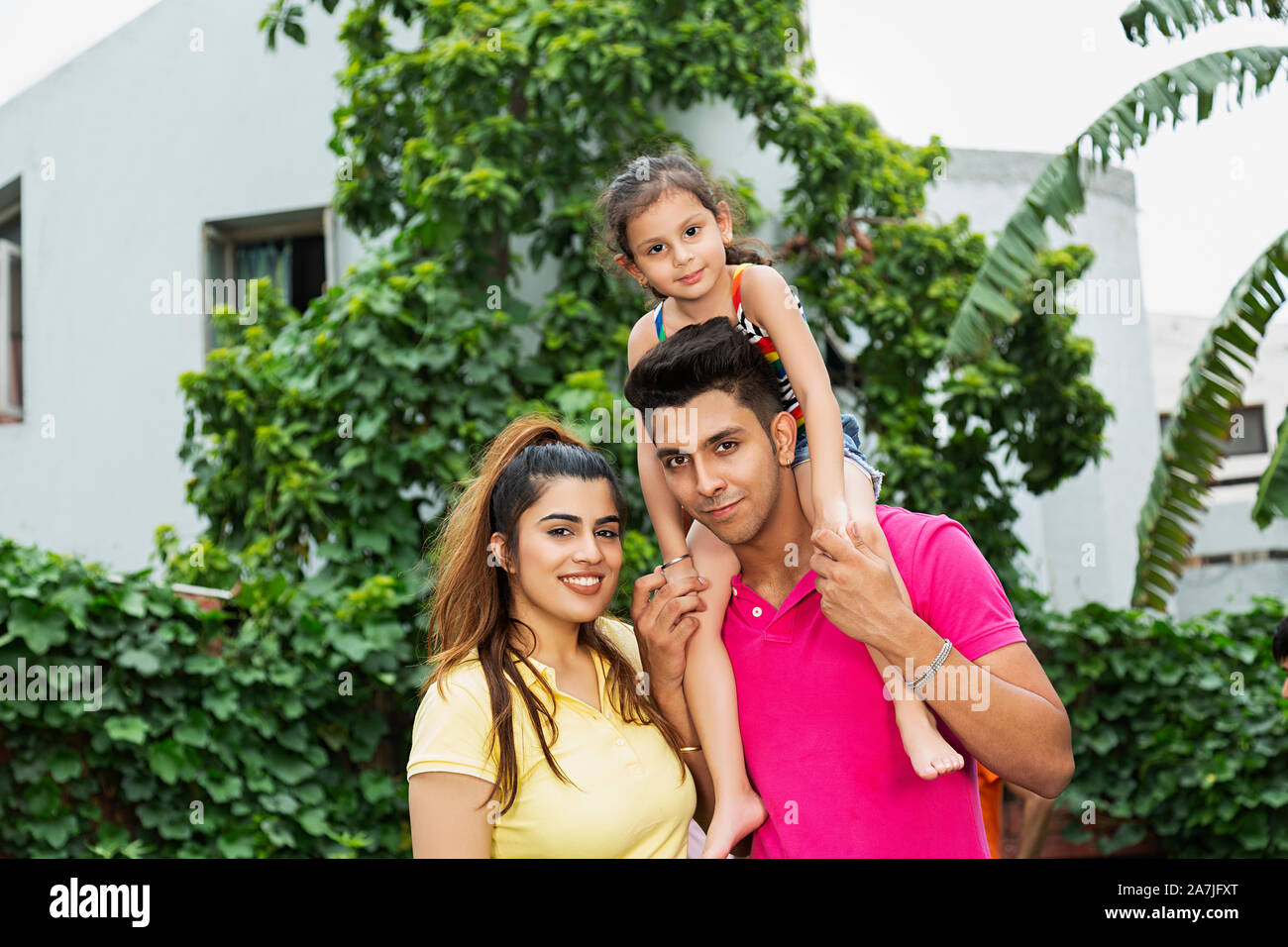 Glückliche junge Familie Vater und Mutter, seine junge Tochter auf seinen Schultern, während Sie im Innenhof in der Nähe von Ihrem Haus Stockfoto