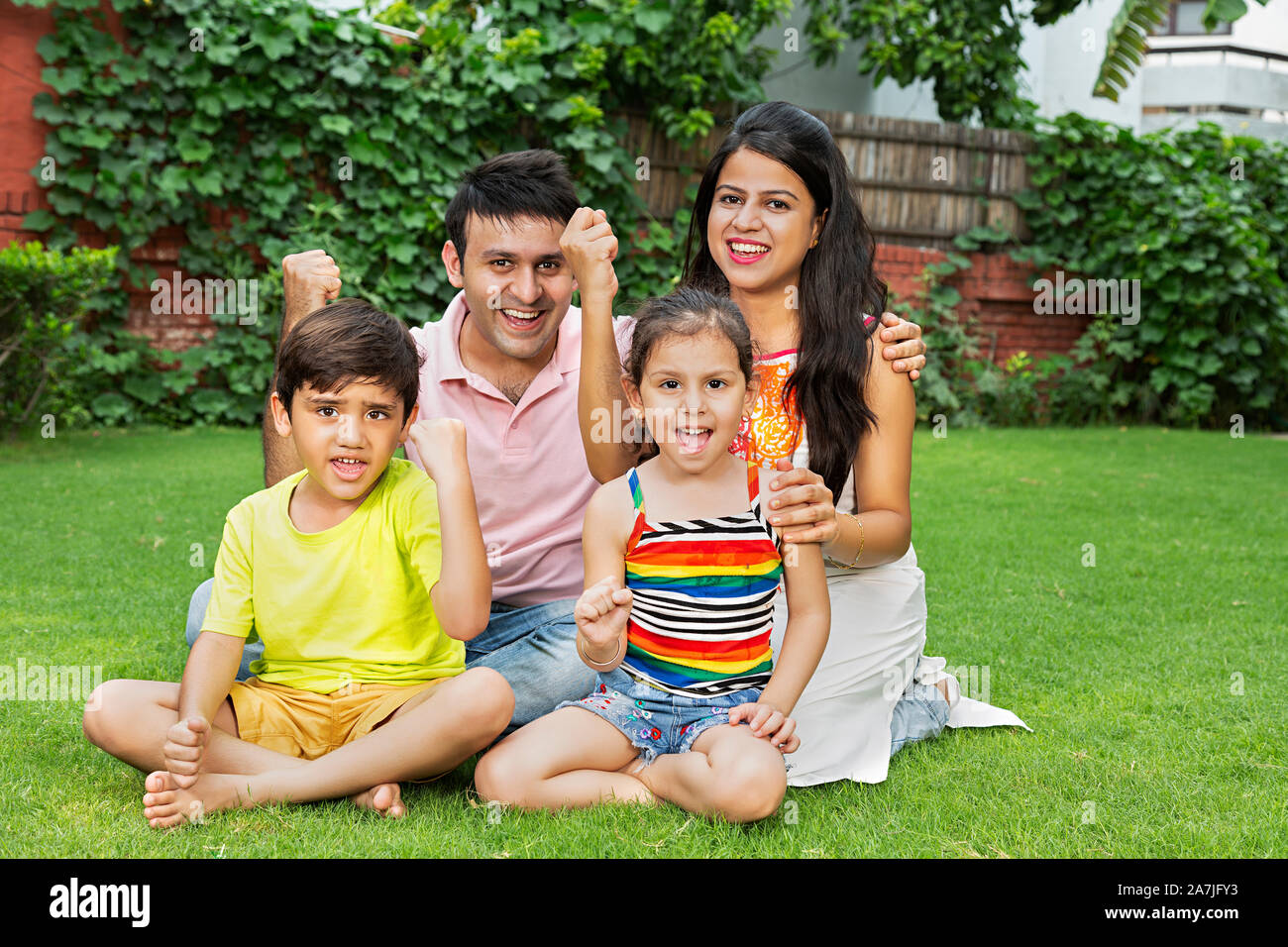 Happy-Family Eltern und zwei Kinder Sohn Tochter sitzen-auf-Gras und Fäuste - hand Erfolg feiern in - Garten Stockfoto