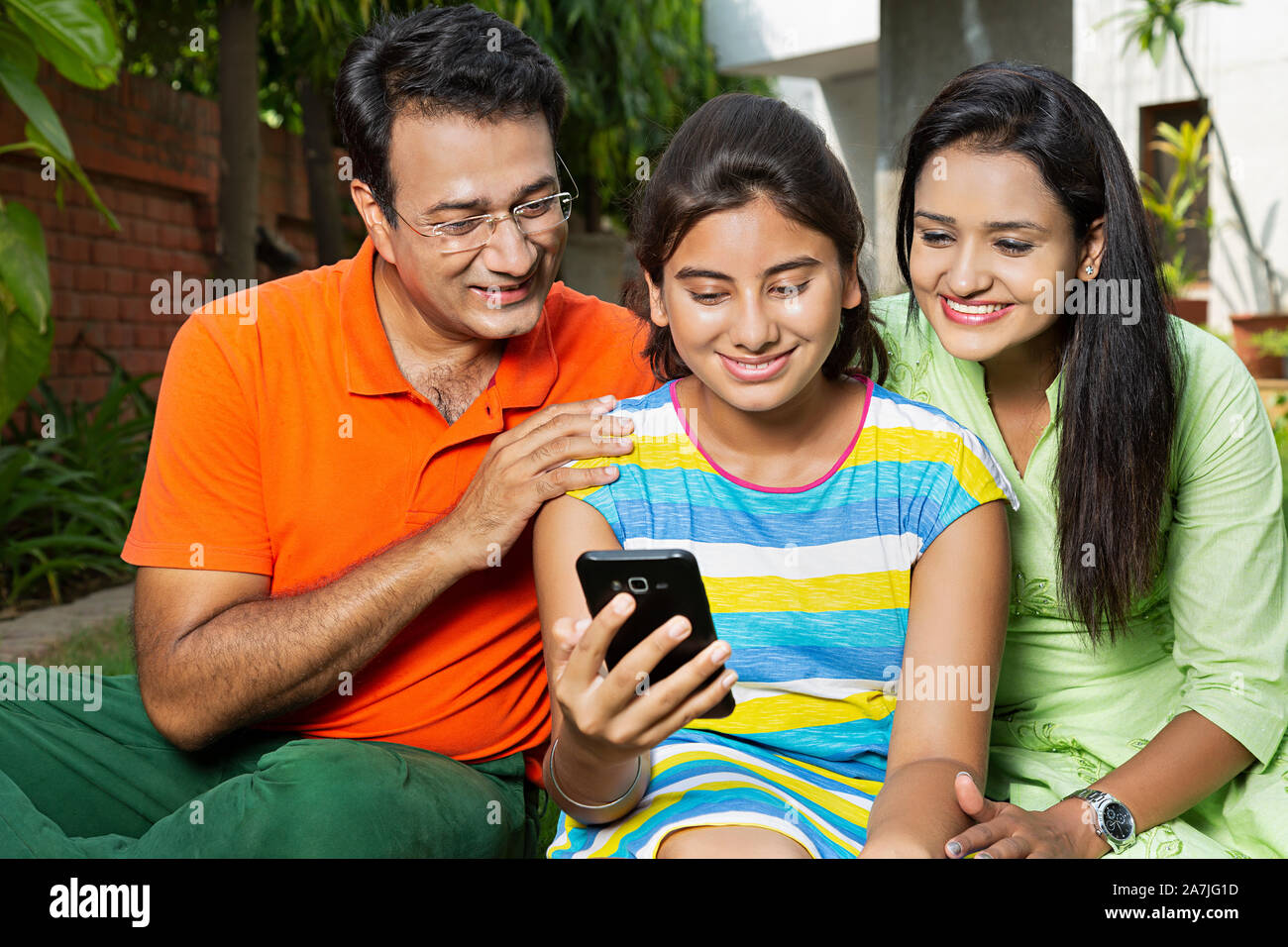 Glückliche Familie Eltern und jungen Erwachsenen Tochter sitzen und lesen At-Courtyard Text-Message auf dem Smartphone Stockfoto