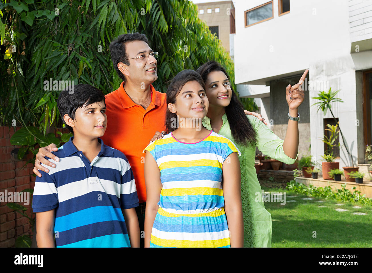 Glückliche Familie Eltern und zwei Kinder zusammen und verweist auf irgendwo in-Hof in der Nähe von Ihrem Haus Stockfoto