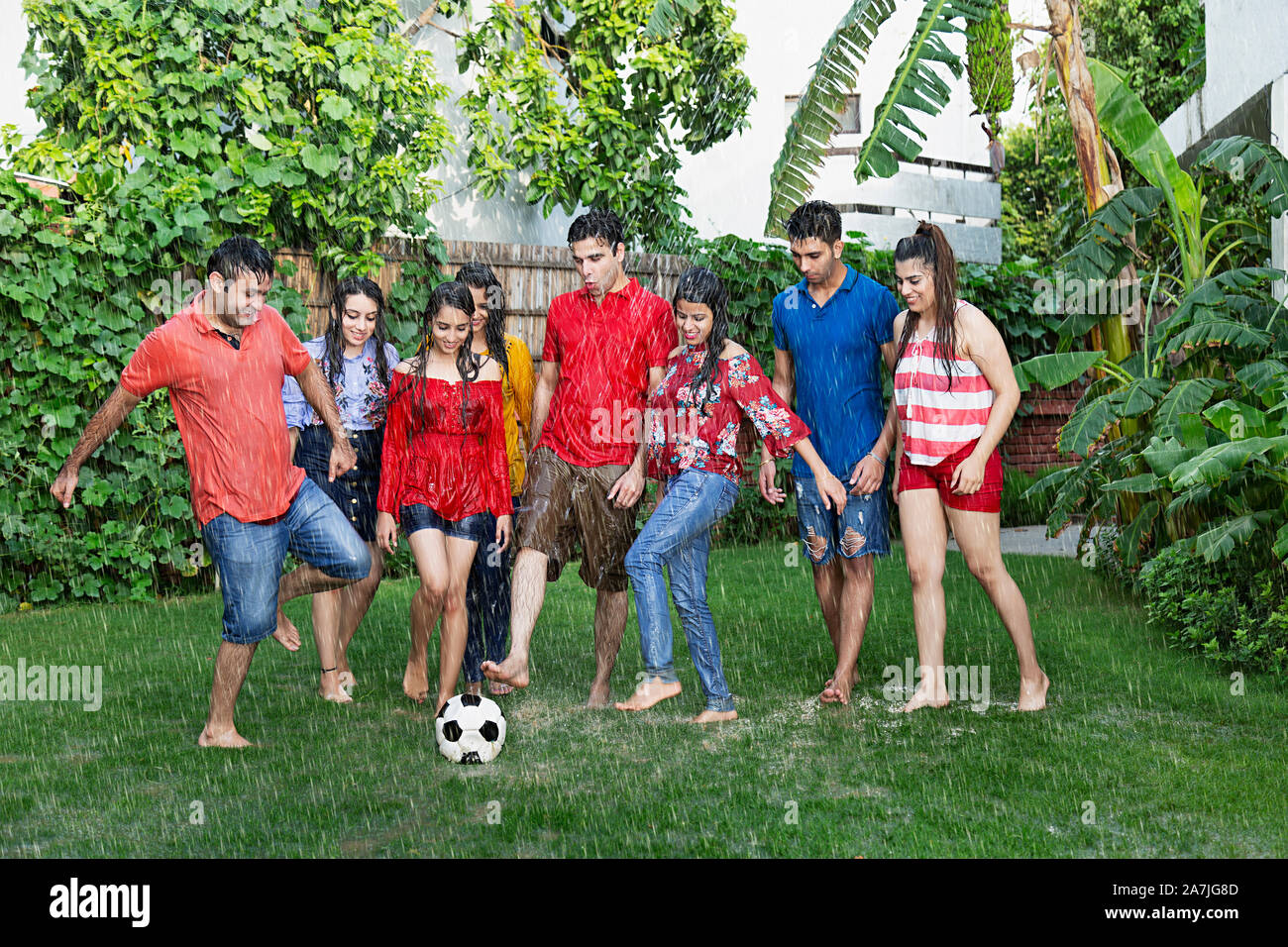 Group-Of Erwachsenen Freunde Männer und Frauen Fußball spielen und Spaß in Regen im Innenhof ihres Hauses Stockfoto