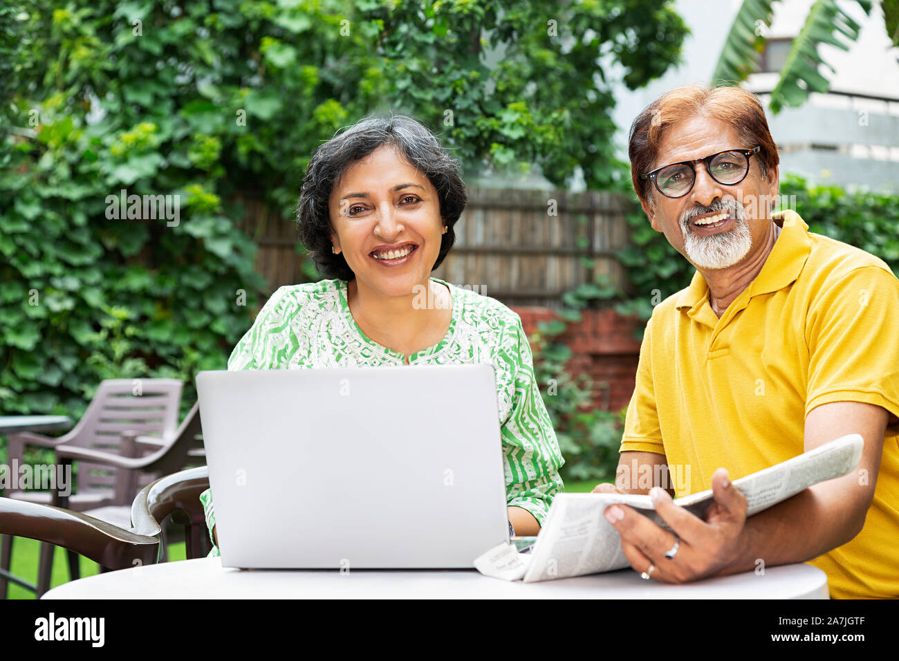 Gerne alte Paar Männliche und Weibliche mit Laptop und lesen Zeitung im Innenhof Ihres Hauses Stockfoto