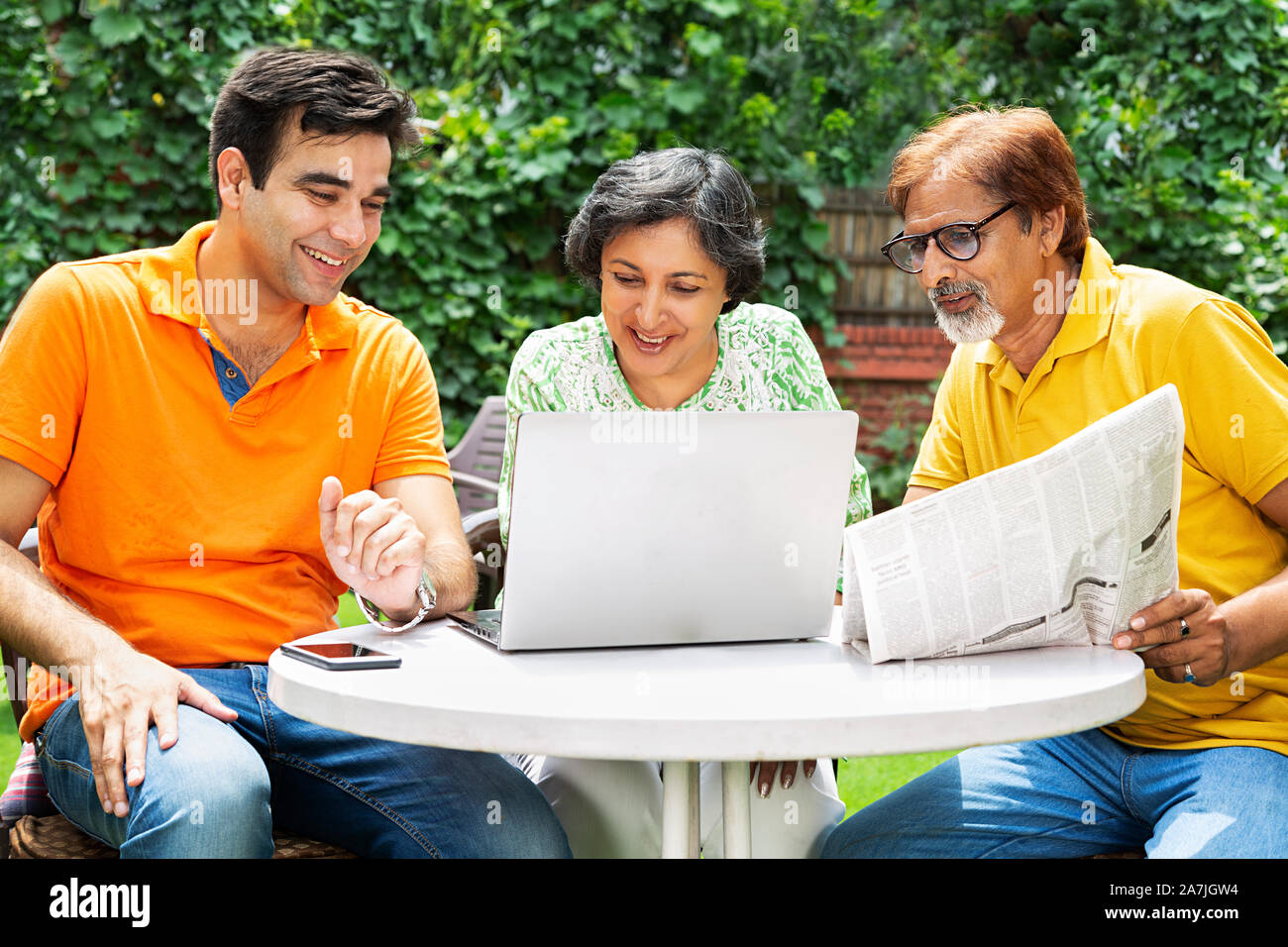 Glückliche Familie Sitzen - im Garten zu Hause Senior Vater und Mutter erwachsener Sohn mit Laptop mit Zeitung in - Morgen Stockfoto
