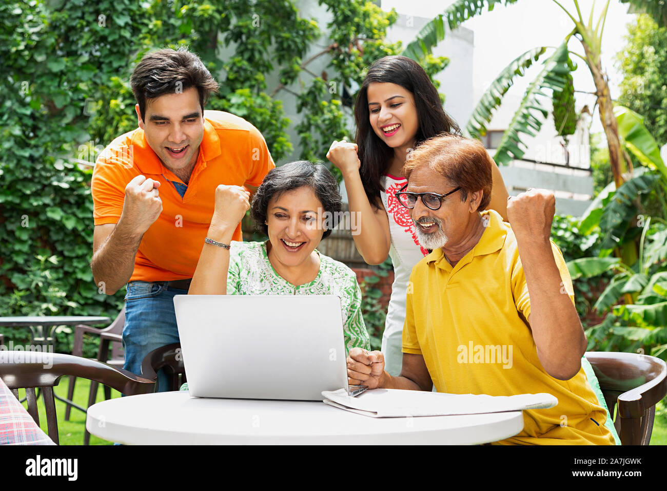 Gerne indische Familie Eltern und Erwachsene Kinder - am Laptop Bildschirm Fäuste hand Erfolge feiern im Garten. Stockfoto