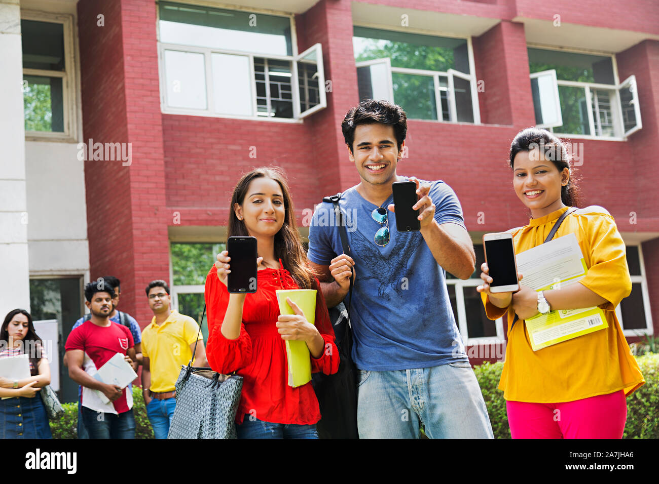 Drei junge Studenten Freunde gemeinsam mit Smartphone und People-In - The-Background At-Campus Gebäude Stockfoto