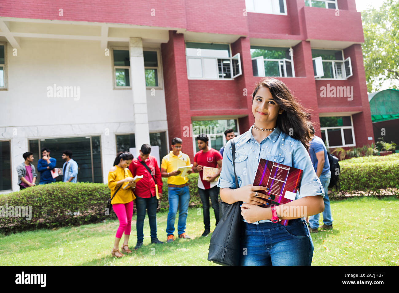 Junge Mädchen Student Holding Buch und Studenten Im-ohr-Hintergrund In-Outside Campus Gebäude Stockfoto