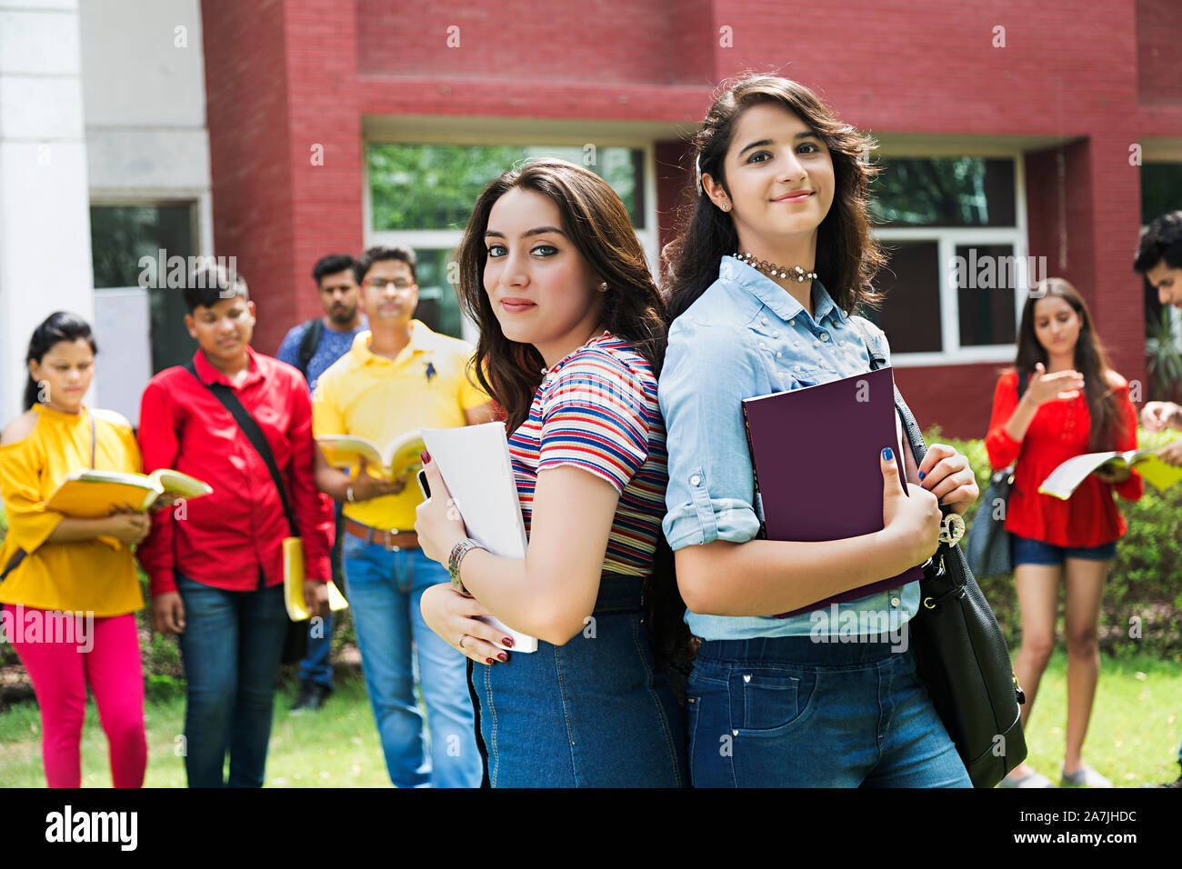 Zwei Teenager Girls College Studenten Freunde Holding Buch Rücken-an-Rücken mit Klassenkameraden im Hintergrund At-Campus Stockfoto