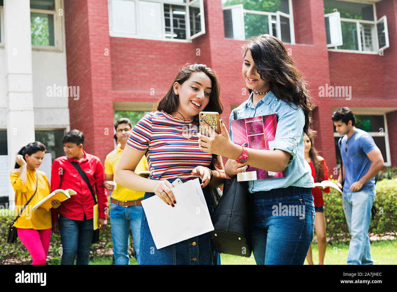 Zwei Teenager Girls College Student Freunde lesen Text-Message Mobile-Phone mit Studenten im Hintergrund stehend auf dem Campus Stockfoto