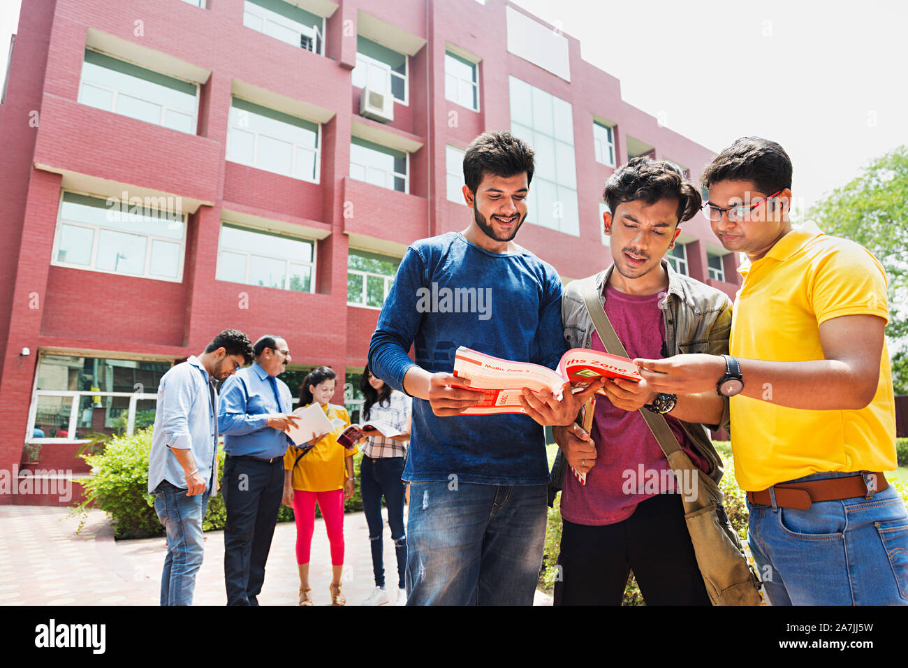 Drei College jungen Studenten Freunde lesen Buch zusammen mit People-In - Hintergrund At-Campus Gebäude Stockfoto