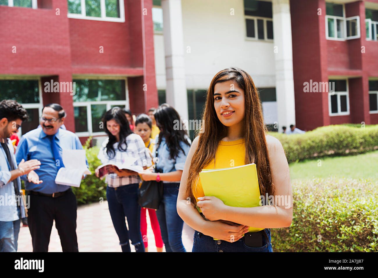 Junge weibliche Studenten Holding Buch mit Studenten und Lehrer in den Hintergrund In-Outside Campus Gebäude Stockfoto