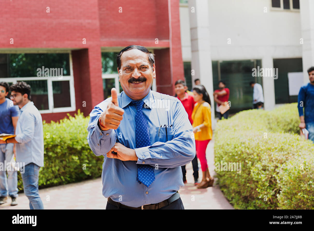 Indische älterer männlichen College Professor angezeigt Thumbs-up mit Students-In - The-Background In-Outside Campus Gebäude Stockfoto