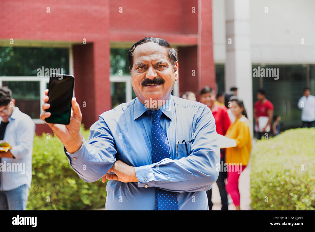 Lächelnd Senior - männliche College Professor zeigt mit Students-In Mobile-Phone-The-Background In-Outside Campus Gebäude Stockfoto