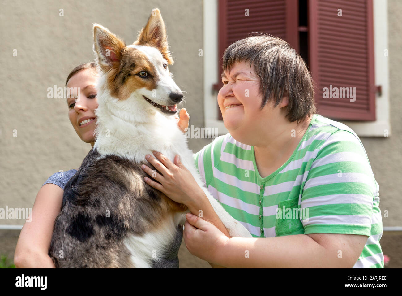 Geistig behinderte Frau vor einem Haus hält ihren Hund, Freundin oder Trainer neben Stockfoto