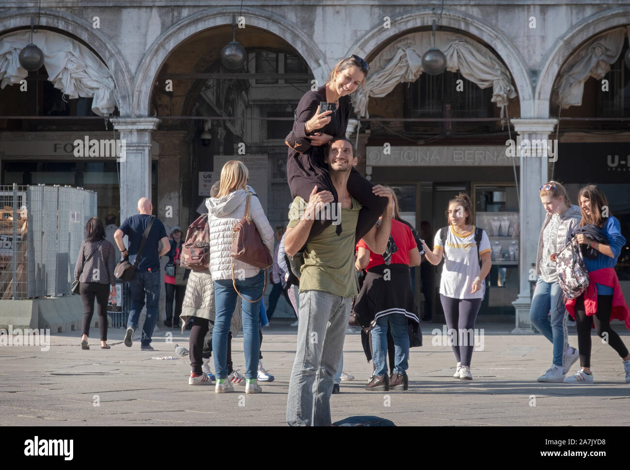 Ein glückliches Paar Blick auf Handy Foto in Piazza San Marco in Venedig, Italien. Die Frau ist auf den Schultern des Mannes sitzt. Stockfoto