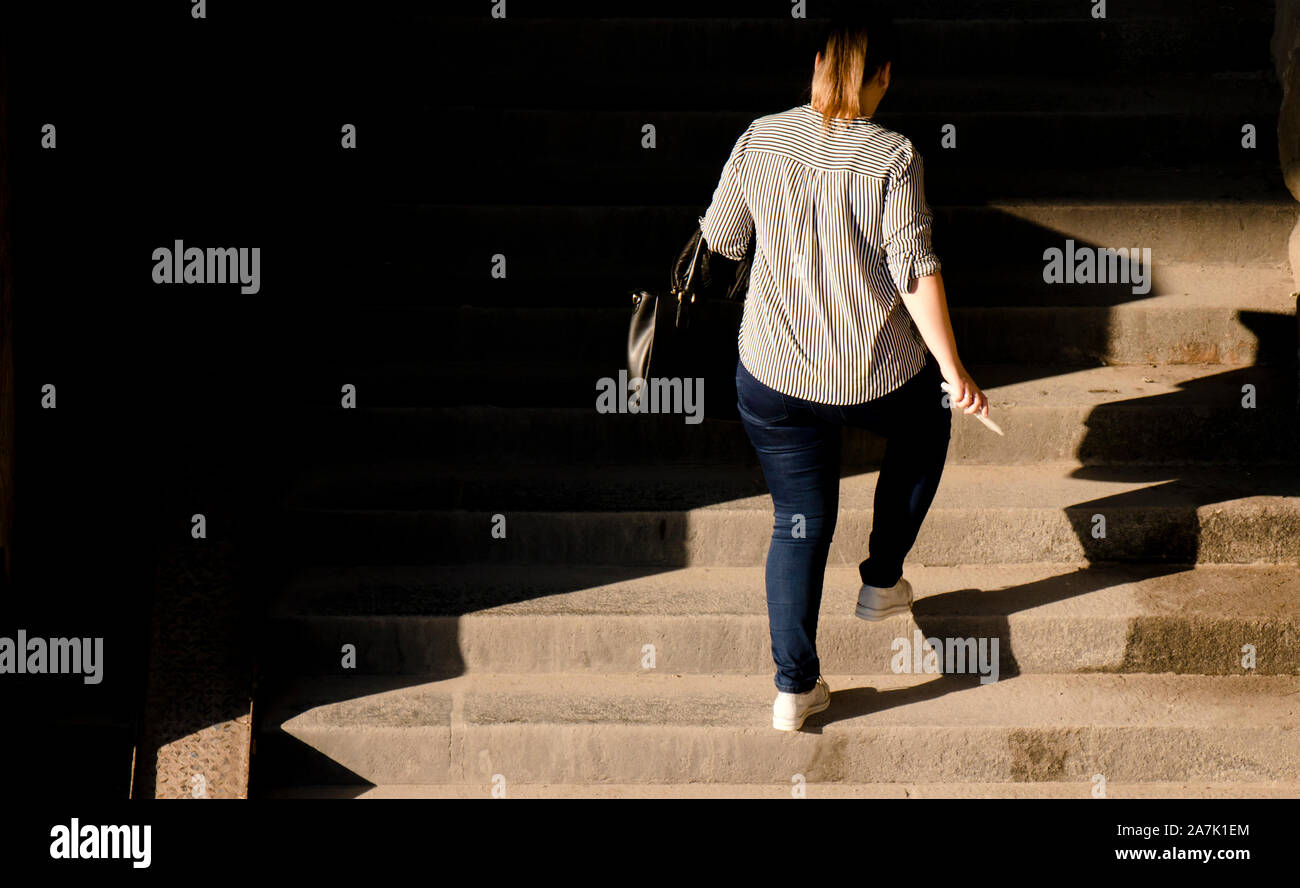 Eins plus größe Frau, die zu Fuss öffentliche Treppe im Sonnenlicht und Schatten, von hinten Stockfoto
