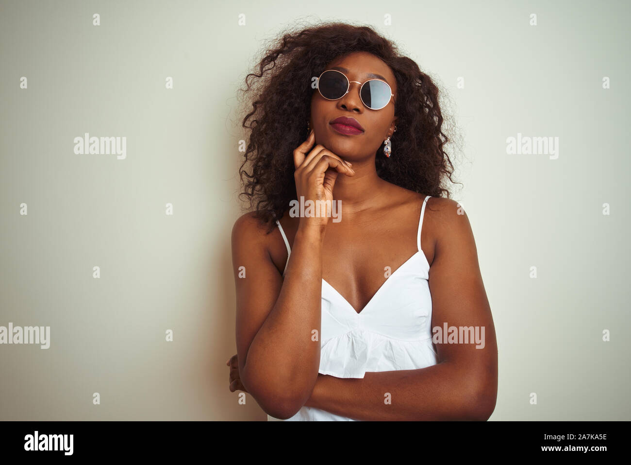 Junge afrikanische amerikanische Frau in T-Shirt und Sonnenbrille über isoliert weißer Hintergrund mit der Hand am Kinn über die Frage nachdenken, nachdenklich expressi Stockfoto