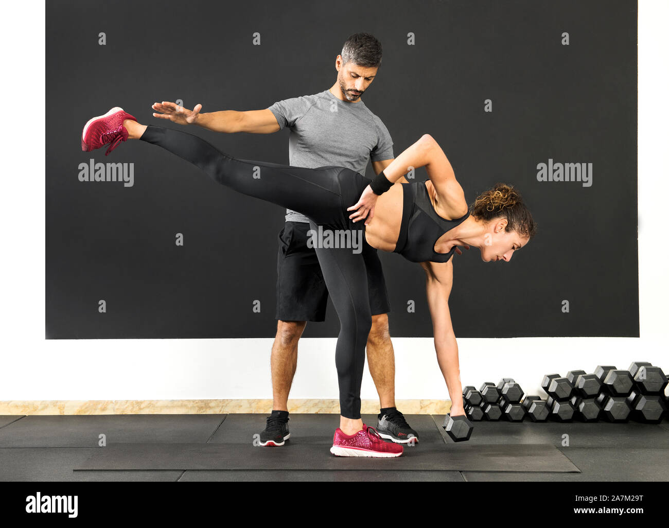 Athletische Frau tun, ein einzelnes Bein Kreuzheben mit einer Hantel, Gewicht, unterstützt von einem männlichen Personal Trainer in einer Turnhalle in einem Gesundheit und Fitness Concept Stockfoto